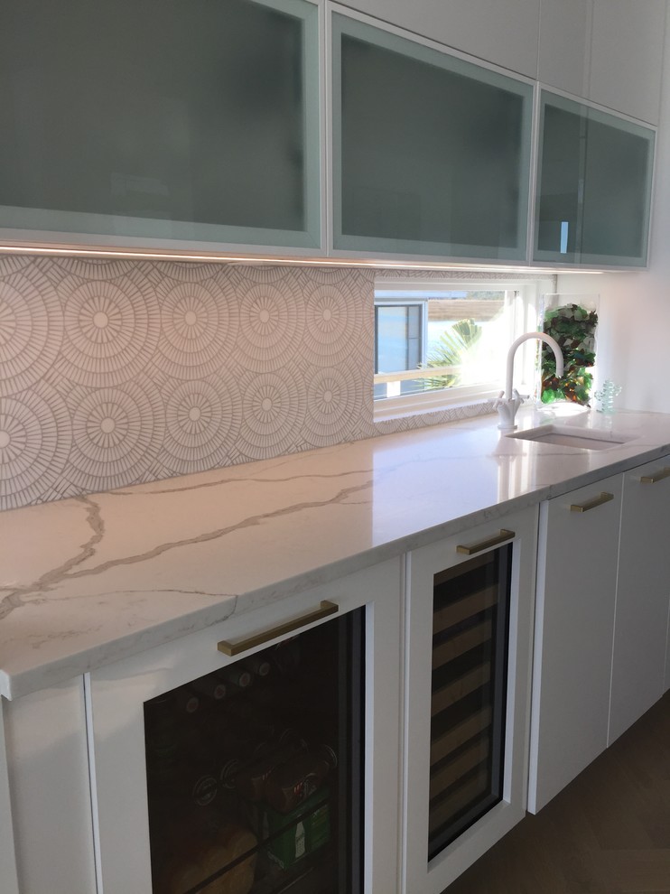 Mid-sized contemporary single-wall kitchen in Orange County with a single-bowl sink, flat-panel cabinets, white cabinets, marble benchtops, white splashback and light hardwood floors.