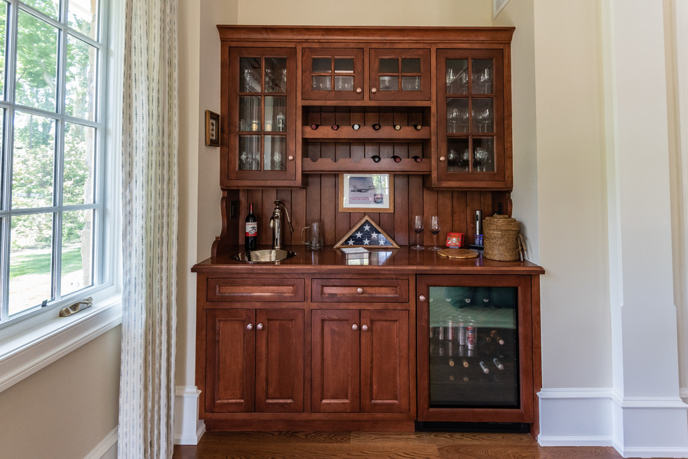 Small transitional single-wall wet bar in Philadelphia with a drop-in sink, recessed-panel cabinets, brown cabinets, wood benchtops, brown splashback, timber splashback, medium hardwood floors, brown floor and brown benchtop.