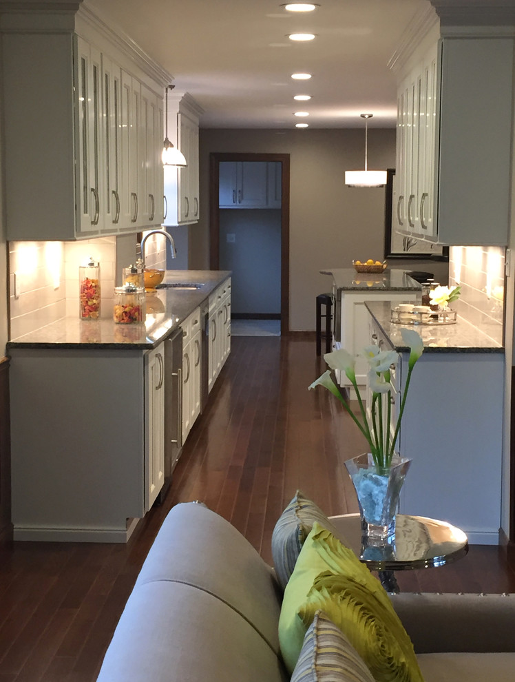 Inspiration for a transitional galley dark wood floor kitchen remodel with an undermount sink, flat-panel cabinets, white cabinets, granite countertops, white backsplash, porcelain backsplash, stainless steel appliances and an island
