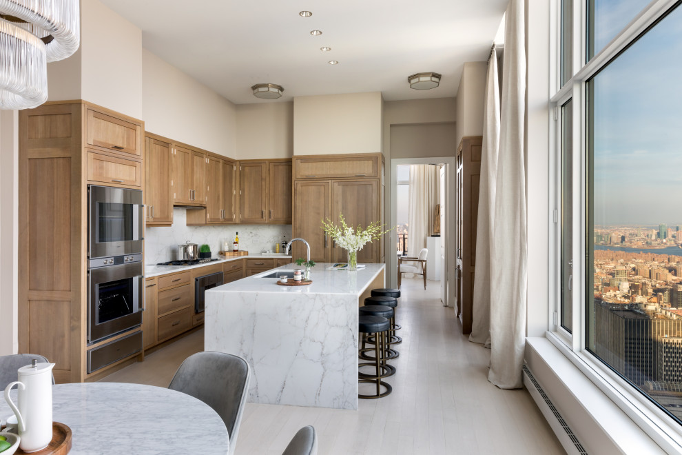 This is an example of a large transitional u-shaped separate kitchen in New York with an undermount sink, recessed-panel cabinets, light wood cabinets, marble benchtops, white splashback, marble splashback, panelled appliances, light hardwood floors, with island, beige floor and white benchtop.