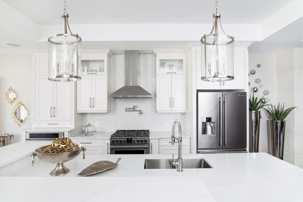 Inspiration for a transitional galley tray ceiling kitchen remodel with an undermount sink, recessed-panel cabinets, white cabinets, white backsplash, stainless steel appliances, an island and white countertops