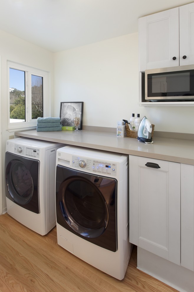 Inspiration for a mid-sized traditional single-wall dedicated laundry room in San Francisco with recessed-panel cabinets, white cabinets, white walls, light hardwood floors and a side-by-side washer and dryer.
