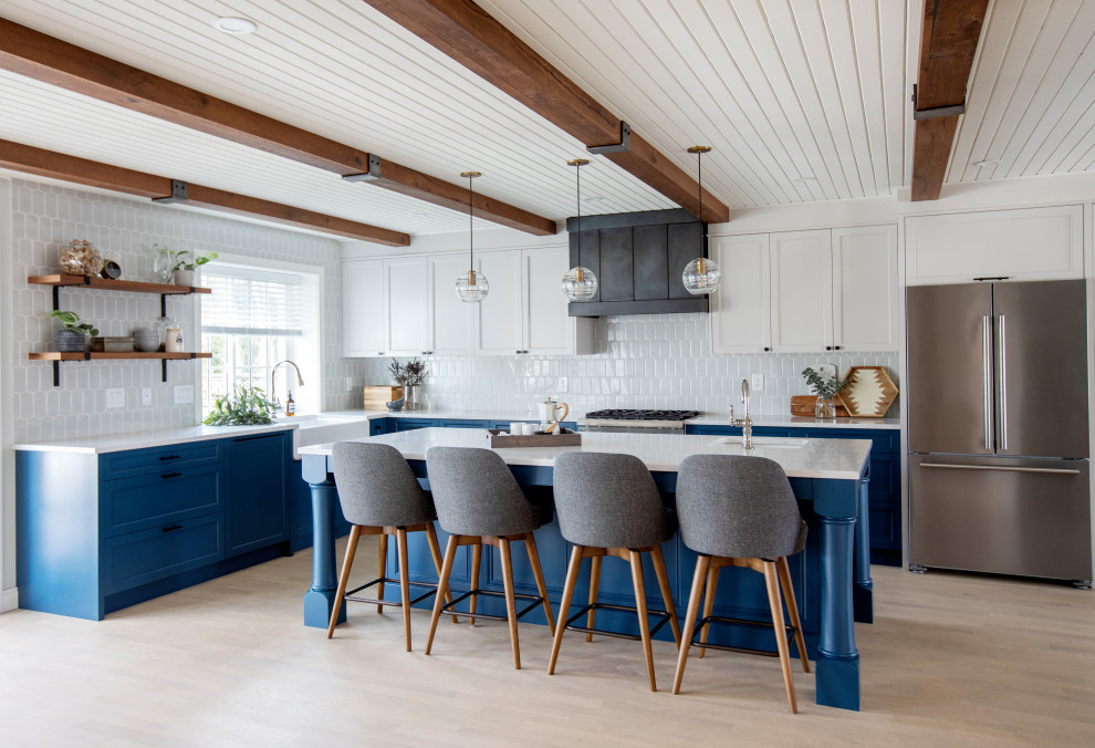 Photo of a country l-shaped kitchen in Vancouver with a farmhouse sink, shaker cabinets, blue cabinets, grey splashback, stainless steel appliances, light hardwood floors, with island, beige floor, white benchtop, exposed beam and timber.