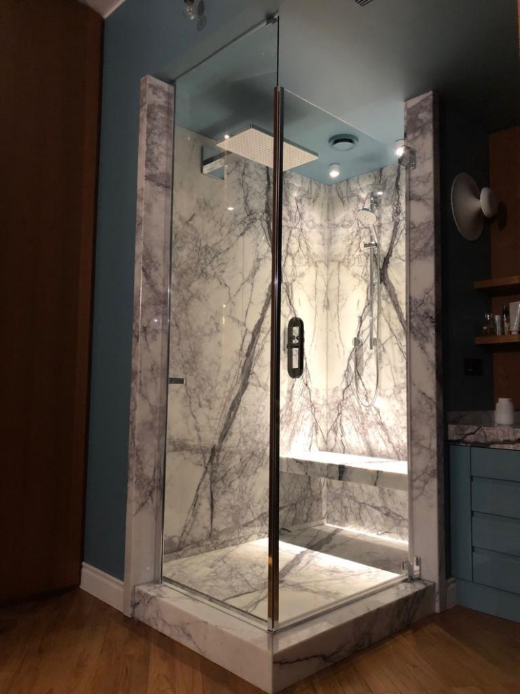 Photo of a mid-sized eclectic master wet room bathroom in Rome with beaded inset cabinets, turquoise cabinets, a wall-mount toilet, blue walls, medium hardwood floors, a vessel sink, marble benchtops, brown floor, a hinged shower door and grey benchtops.
