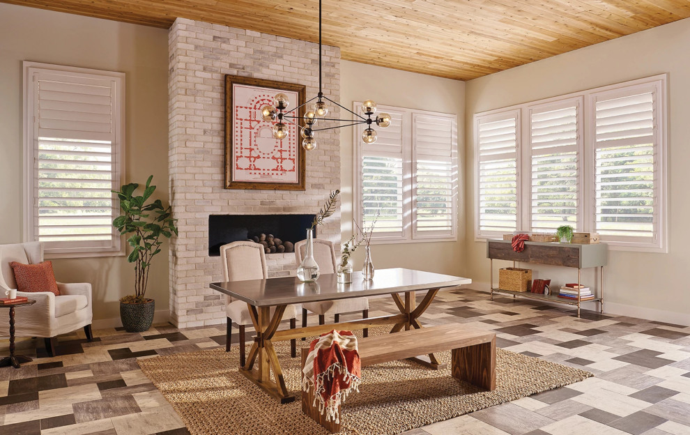 Cette image montre une salle à manger ouverte sur le salon traditionnelle de taille moyenne avec un mur beige, un sol en linoléum, une cheminée standard, un manteau de cheminée en brique, un sol beige et un plafond en bois.