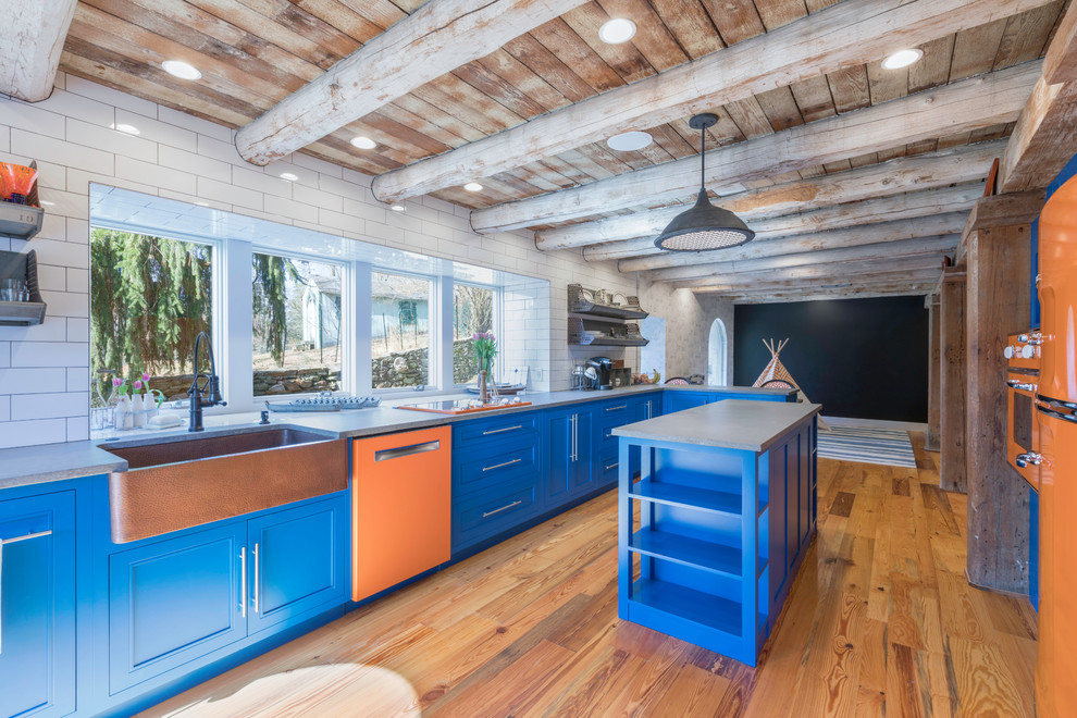 Country galley kitchen in Philadelphia with a farmhouse sink, blue cabinets, concrete benchtops, white splashback, subway tile splashback, coloured appliances, with island, grey benchtop, recessed-panel cabinets, medium hardwood floors and brown floor.
