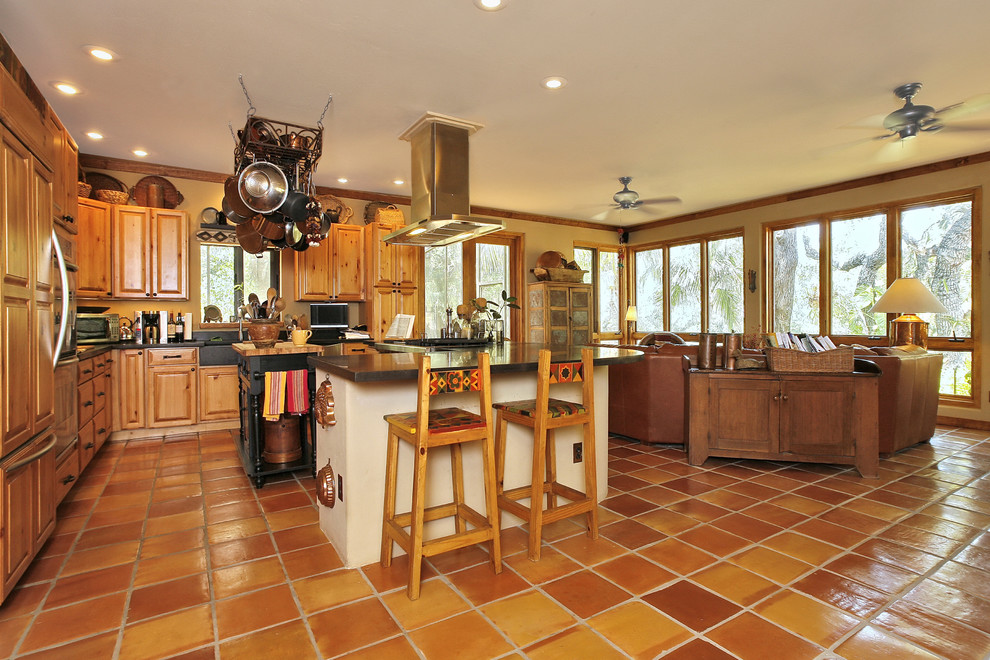 Traditional l-shaped open plan kitchen in Tampa with a farmhouse sink, raised-panel cabinets, light wood cabinets, solid surface benchtops, panelled appliances, terra-cotta floors and with island.