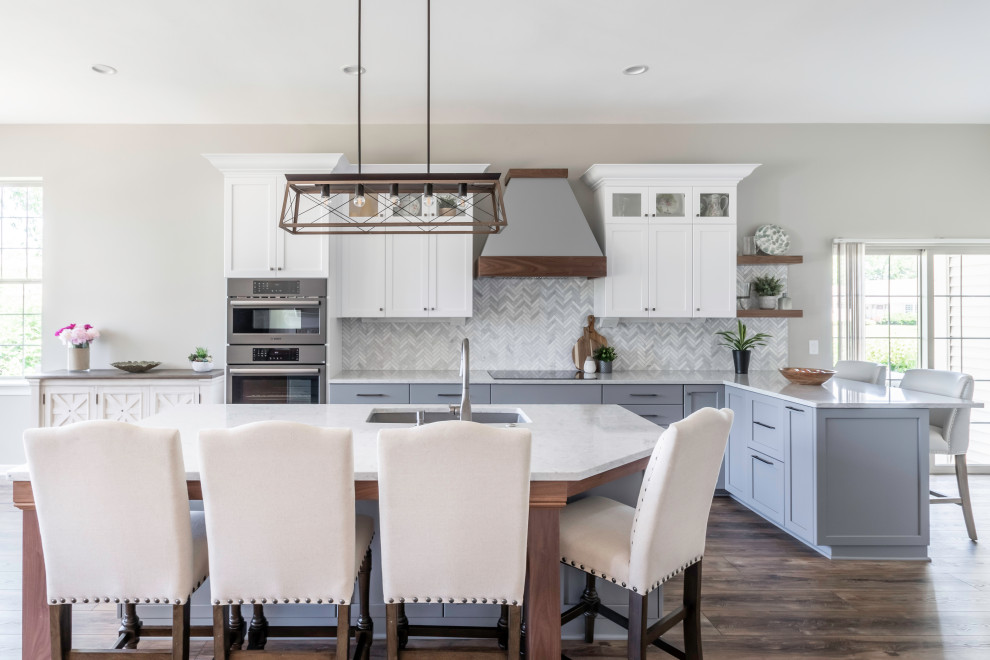 This is an example of a large classic l-shaped open plan kitchen in Milwaukee with a double-bowl sink, shaker cabinets, white cabinets, engineered stone countertops, white splashback, marble splashback, stainless steel appliances, vinyl flooring, an island, brown floors and white worktops.