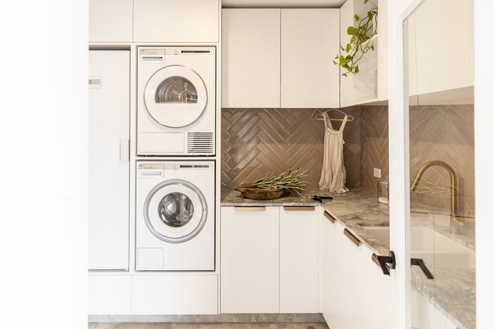 パースにあるお手頃価格の中くらいなコンテンポラリースタイルのおしゃれな洗濯室 (ダブルシンク、白いキャビネット、大理石カウンター、ピンクのキッチンパネル、サブウェイタイルのキッチンパネル、白い壁、磁器タイルの床、上下配置の洗濯機・乾燥機、マルチカラーのキッチンカウンター) の写真