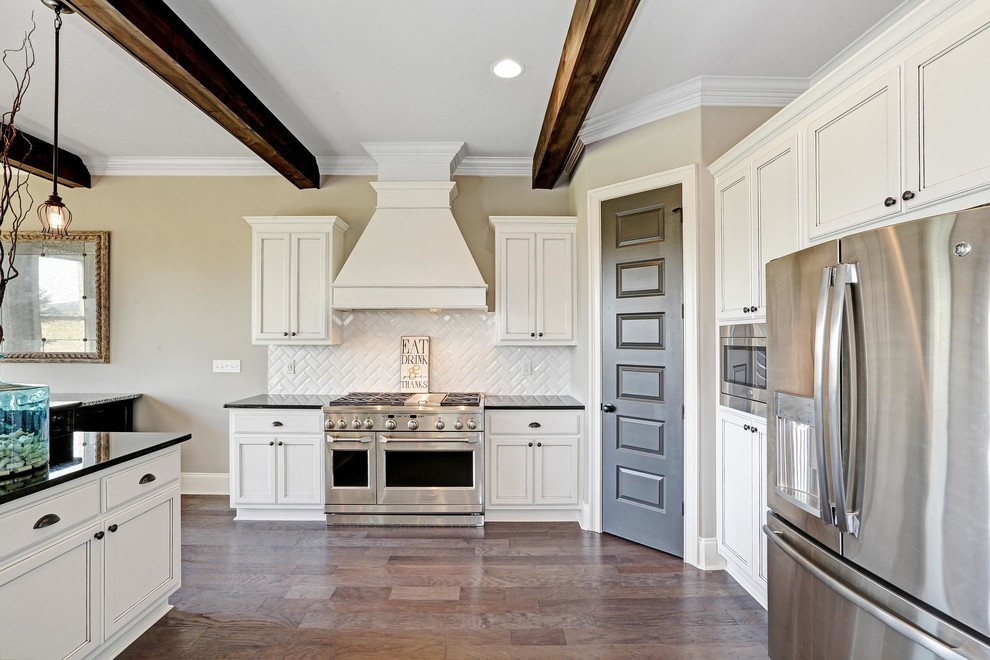 Example of a large transitional l-shaped medium tone wood floor and brown floor open concept kitchen design with a double-bowl sink, recessed-panel cabinets, white cabinets, quartz countertops, white backsplash, subway tile backsplash, stainless steel appliances, an island and black countertops