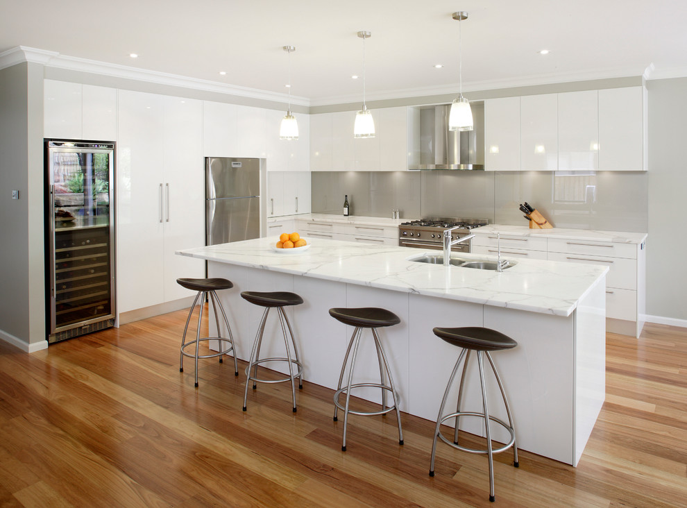 Inspiration for a mid-sized contemporary l-shaped kitchen in Sydney with stainless steel appliances, an undermount sink, white cabinets, marble benchtops, metallic splashback, glass sheet splashback, with island and medium hardwood floors.