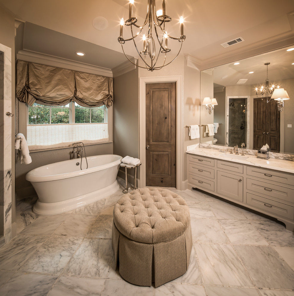 Photo of a mid-sized traditional master bathroom in Houston with white cabinets, a freestanding tub, white tile, recessed-panel cabinets, ceramic tile, beige walls, marble floors, an undermount sink, quartzite benchtops, white floor and a hinged shower door.