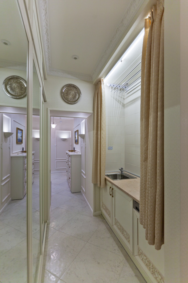 This is an example of a small traditional single-wall utility room in Saint Petersburg with a single-bowl sink, beaded inset cabinets, beige cabinets, solid surface benchtops, beige walls, porcelain floors, a concealed washer and dryer and beige floor.
