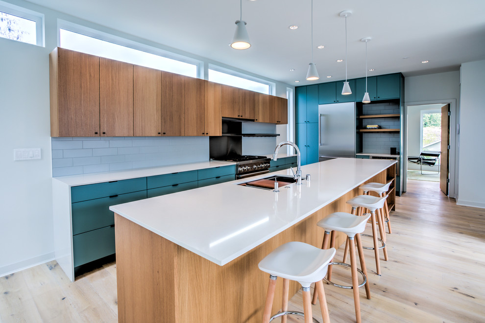 Design ideas for a large contemporary kitchen in Seattle with an undermount sink, flat-panel cabinets, white splashback, stainless steel appliances, light hardwood floors, with island, white benchtop, turquoise cabinets, subway tile splashback and beige floor.