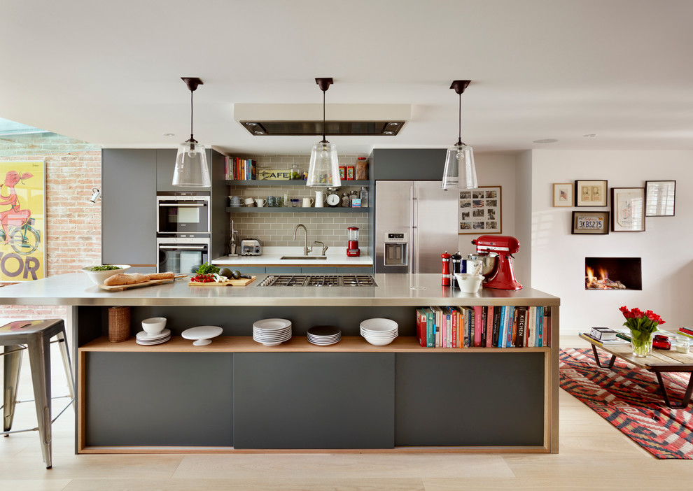 This is an example of a large contemporary galley open plan kitchen in London with with island, flat-panel cabinets, grey cabinets, quartz benchtops, grey splashback, subway tile splashback, stainless steel appliances, an undermount sink and light hardwood floors.