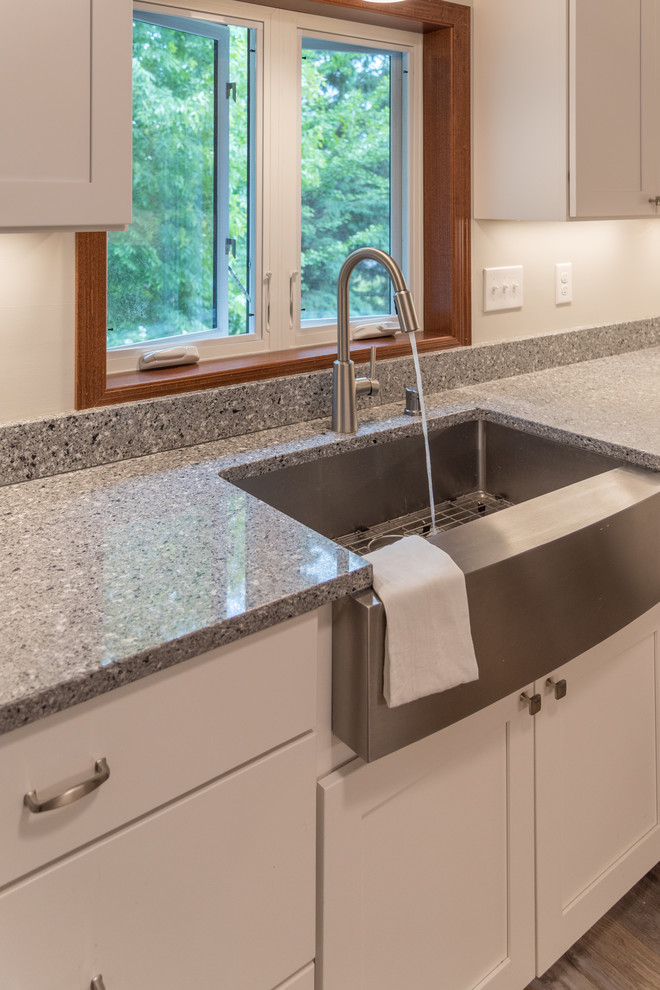 Large transitional u-shaped light wood floor and brown floor enclosed kitchen photo in Minneapolis with a farmhouse sink, shaker cabinets, white cabinets, granite countertops, stainless steel appliances, a peninsula and gray countertops
