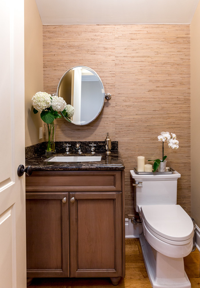 Inspiration for a mid-sized transitional powder room in Los Angeles with beaded inset cabinets, medium wood cabinets, a one-piece toilet, beige walls, medium hardwood floors, an undermount sink, granite benchtops, brown floor and black benchtops.