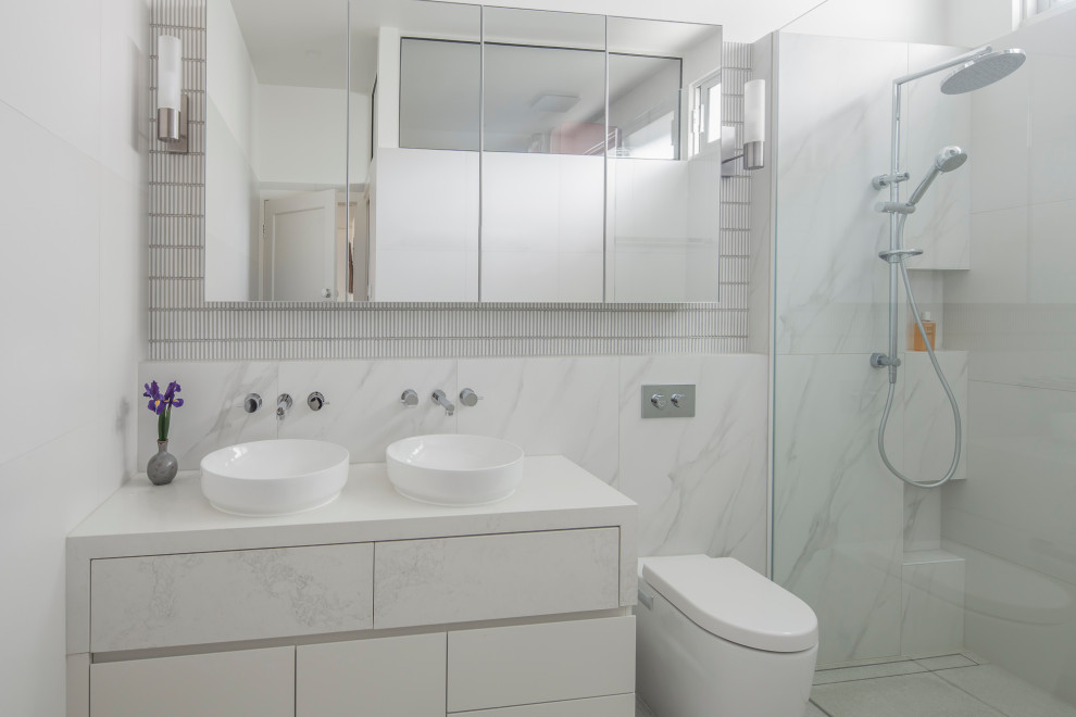 This is an example of a mid-sized contemporary master bathroom in Melbourne with flat-panel cabinets, white cabinets, an open shower, a wall-mount toilet, white tile, ceramic tile, white walls, porcelain floors, a vessel sink, engineered quartz benchtops, white floor, an open shower, white benchtops, a niche, a double vanity and a built-in vanity.
