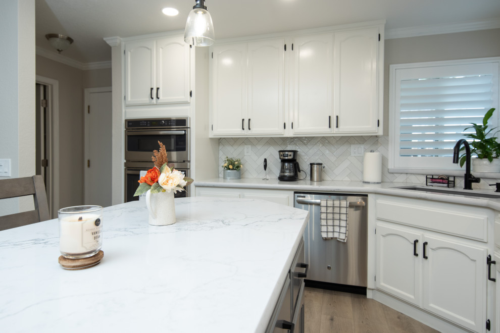 This is an example of a modern eat-in kitchen in Sacramento with an undermount sink, white cabinets, quartz benchtops, white splashback, ceramic splashback, stainless steel appliances, with island and white benchtop.
