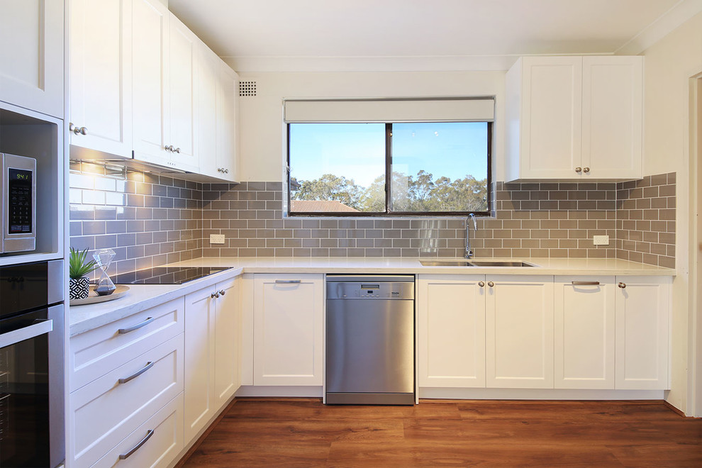 Photo of a mid-sized country u-shaped separate kitchen in Sydney with an undermount sink, shaker cabinets, white cabinets, quartz benchtops, ceramic splashback, stainless steel appliances, laminate floors and no island.