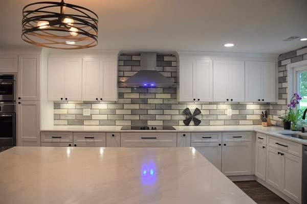 Inspiration for a large transitional l-shaped medium tone wood floor open concept kitchen remodel in Baltimore with a single-bowl sink, shaker cabinets, white cabinets, quartz countertops, gray backsplash, subway tile backsplash, stainless steel appliances, an island and white countertops