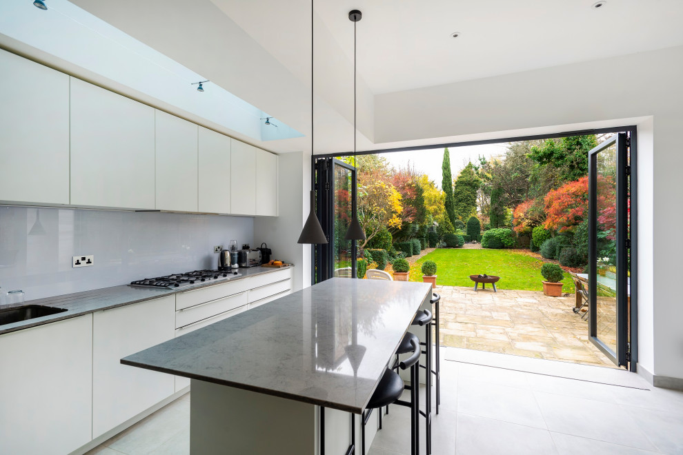 Inspiration for a large contemporary l-shaped open plan kitchen in London with an integrated sink, flat-panel cabinets, white cabinets, composite countertops, grey splashback, integrated appliances, medium hardwood flooring, an island and grey worktops.