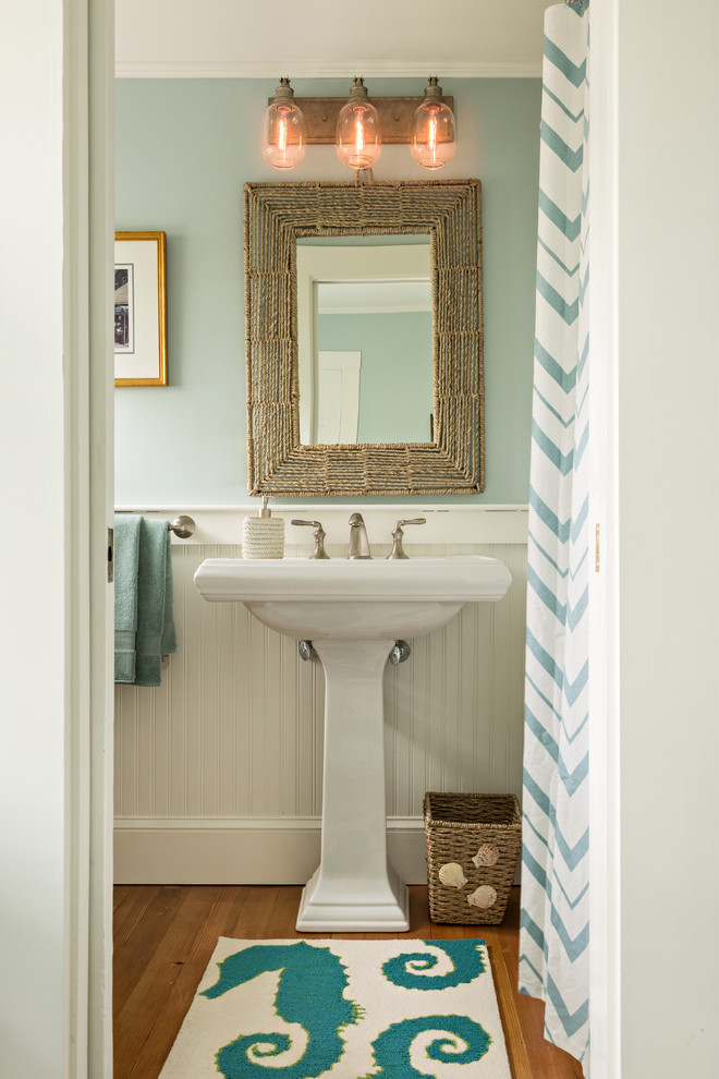 Beach style bathroom in Boston with blue walls, medium hardwood floors, a pedestal sink, brown floor and a shower curtain.