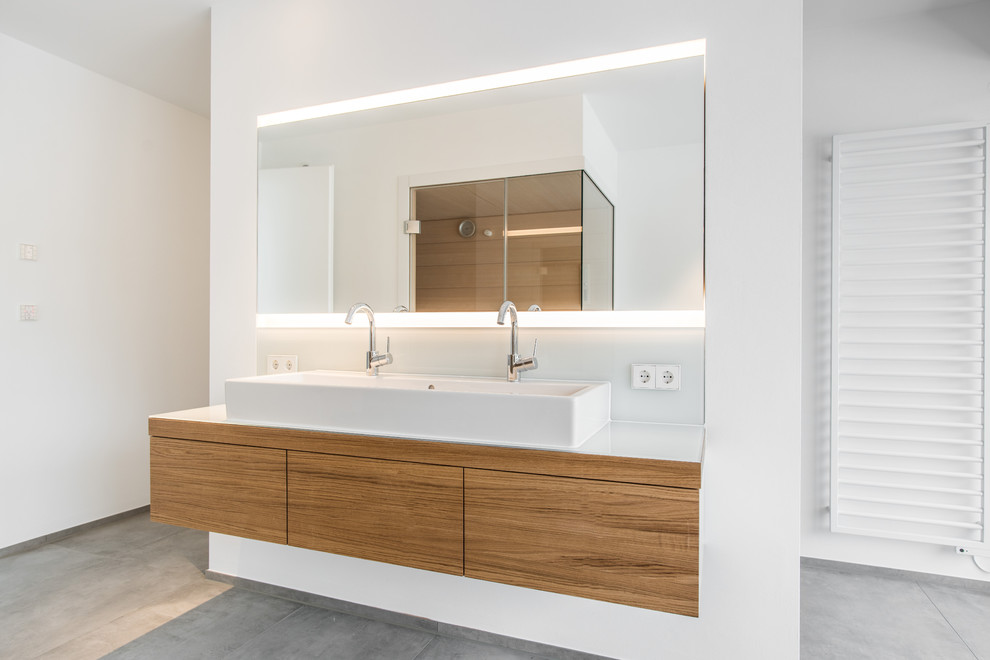This is an example of a mid-sized contemporary bathroom in Stuttgart with flat-panel cabinets, medium wood cabinets, white tile, glass sheet wall, white walls, a vessel sink, grey floor and white benchtops.