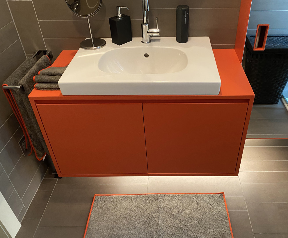 Exempel på ett litet modernt orange oranget badrum med dusch, med släta luckor, orange skåp, en vägghängd toalettstol, grå kakel, porslinskakel, grå väggar, klinkergolv i porslin, ett fristående handfat och grått golv