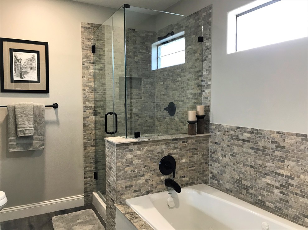 This is an example of a mid-sized country master bathroom in Houston with white cabinets, a drop-in tub, an open shower, travertine, grey walls, laminate floors, a drop-in sink, granite benchtops, brown floor, a hinged shower door and black benchtops.