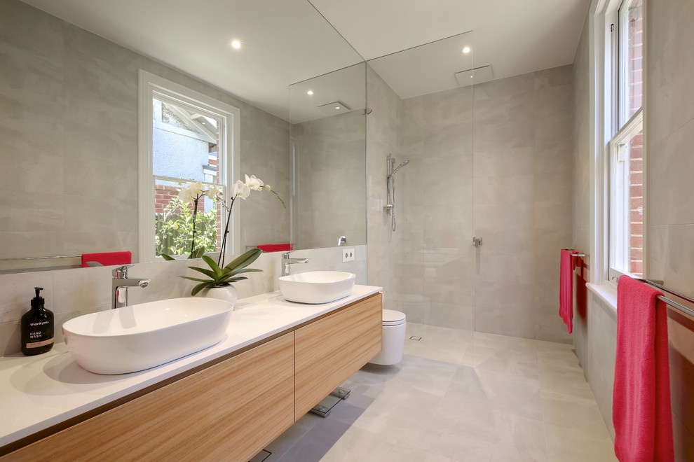 Mid-sized contemporary wet room bathroom in Adelaide with furniture-like cabinets, light wood cabinets, a wall-mount toilet, gray tile, ceramic tile, grey walls, ceramic floors, a console sink, engineered quartz benchtops, grey floor, an open shower and white benchtops.