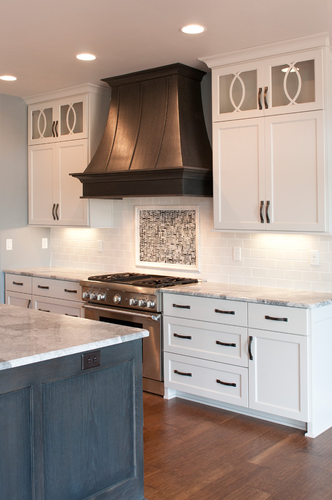 Design ideas for a large contemporary l-shaped kitchen in Milwaukee with an undermount sink, recessed-panel cabinets, white cabinets, granite benchtops, white splashback, ceramic splashback, stainless steel appliances, medium hardwood floors and with island.
