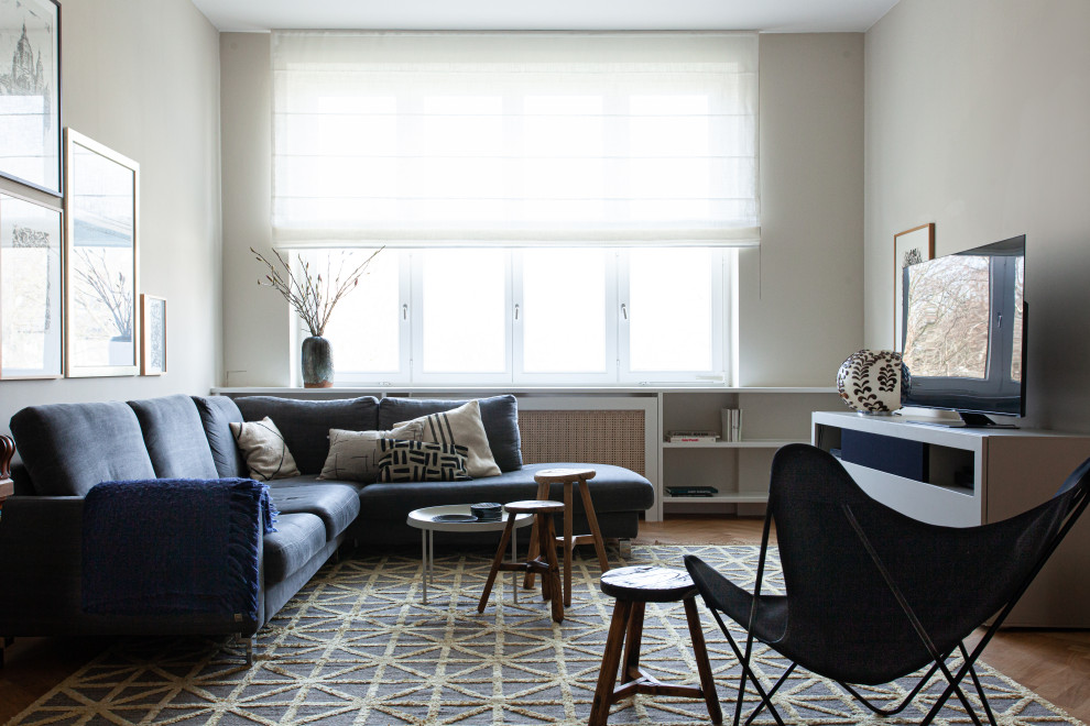 Modernes Wohnzimmer mit grauer Wandfarbe, braunem Holzboden, freistehendem TV und braunem Boden in Berlin