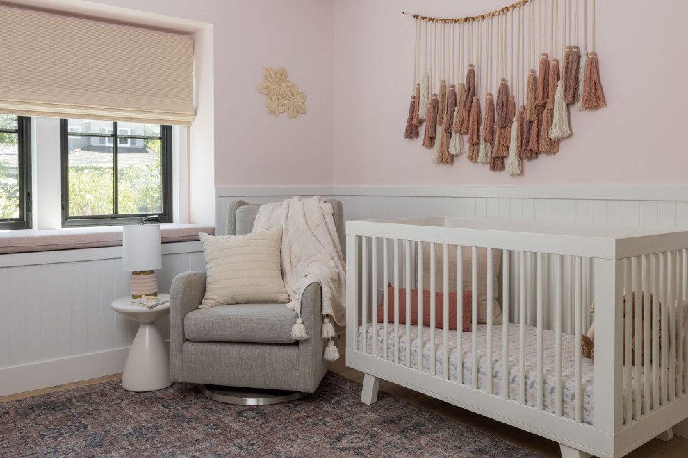 Photo of a medium sized country nursery for girls in San Francisco with pink walls, light hardwood flooring, brown floors and wainscoting.