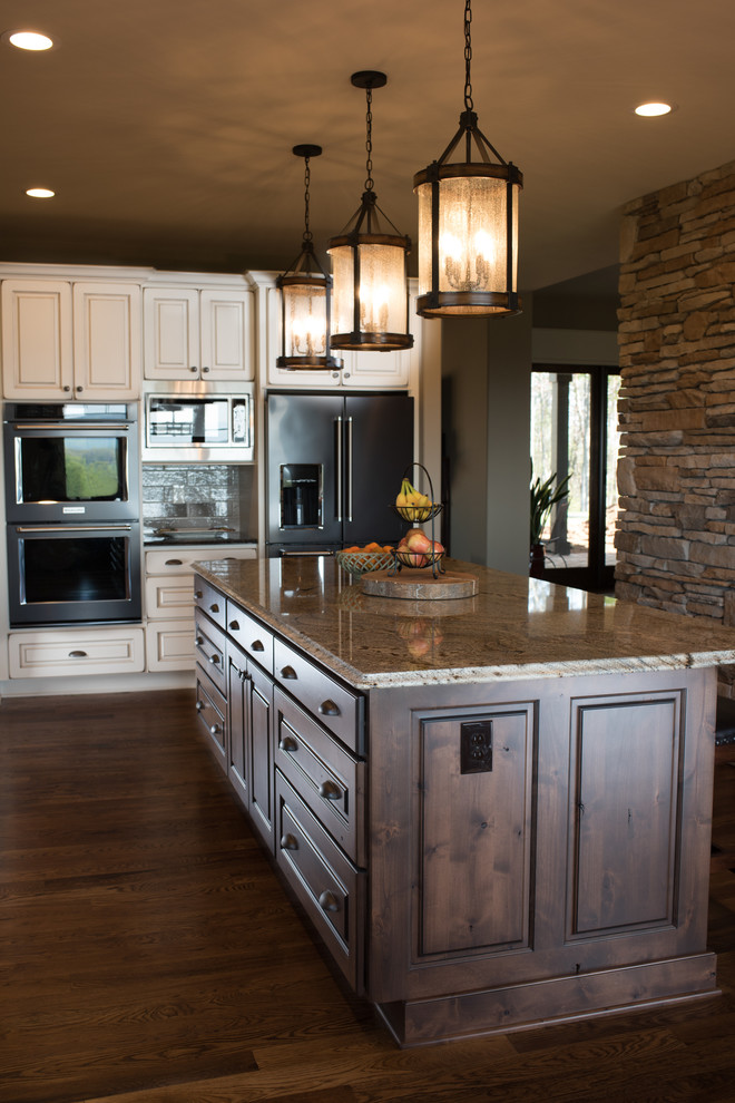 Example of a large mountain style l-shaped dark wood floor and brown floor eat-in kitchen design with a farmhouse sink, raised-panel cabinets, dark wood cabinets, granite countertops, gray backsplash, ceramic backsplash, black appliances and an island