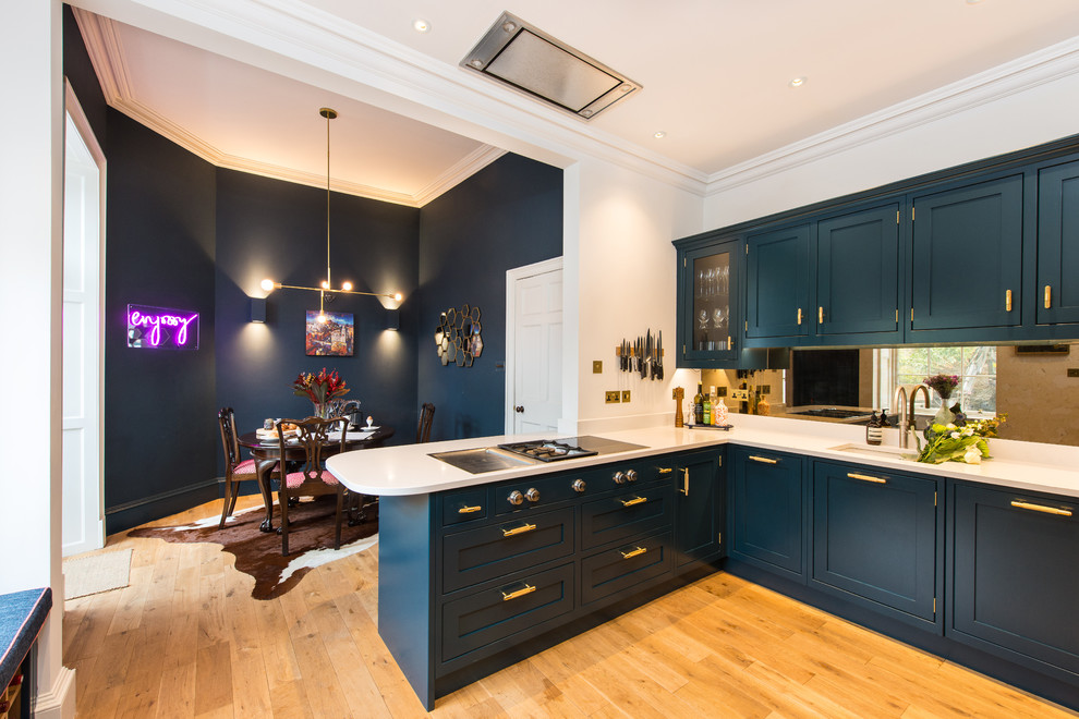 Design ideas for a transitional l-shaped eat-in kitchen in Other with an undermount sink, shaker cabinets, blue cabinets, mirror splashback, medium hardwood floors, a peninsula and white benchtop.