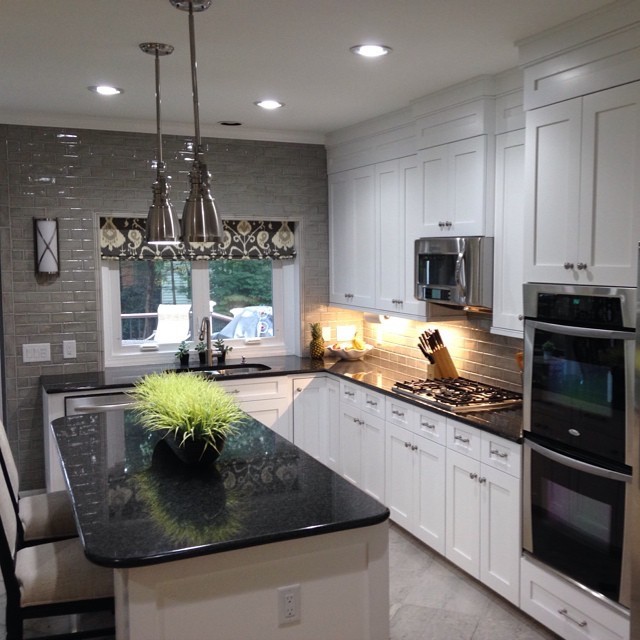 Large transitional l-shaped eat-in kitchen in Charlotte with a double-bowl sink, flat-panel cabinets, white cabinets, granite benchtops, grey splashback, glass tile splashback, stainless steel appliances, ceramic floors and with island.