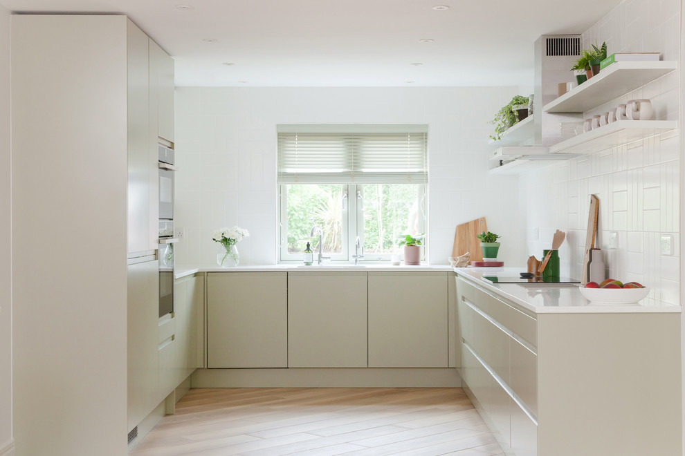 Photo of a scandinavian u-shaped separate kitchen in Cambridgeshire with flat-panel cabinets, beige cabinets, ceramic splashback, panelled appliances, light hardwood floors, no island, beige floor and white benchtop.
