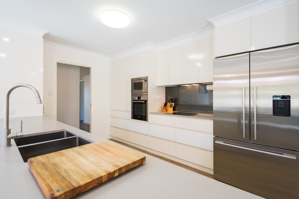 Photo of a large modern galley open plan kitchen in Brisbane with an undermount sink, flat-panel cabinets, beige cabinets, quartz benchtops, grey splashback, glass sheet splashback, stainless steel appliances and with island.