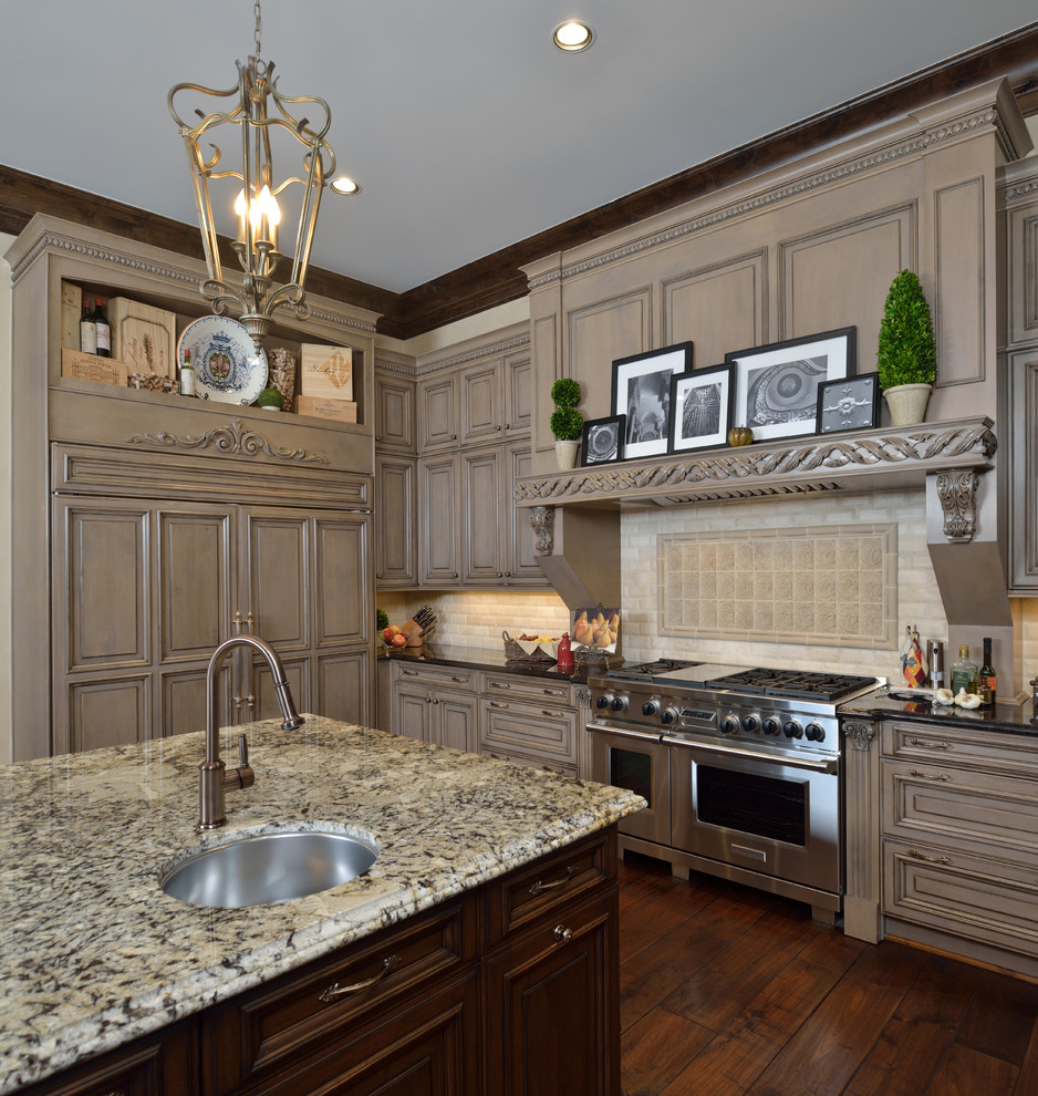 Photo of a large traditional l-shaped open plan kitchen in Houston with a double-bowl sink, grey cabinets, granite benchtops, beige splashback, stone tile splashback, panelled appliances, medium hardwood floors and with island.