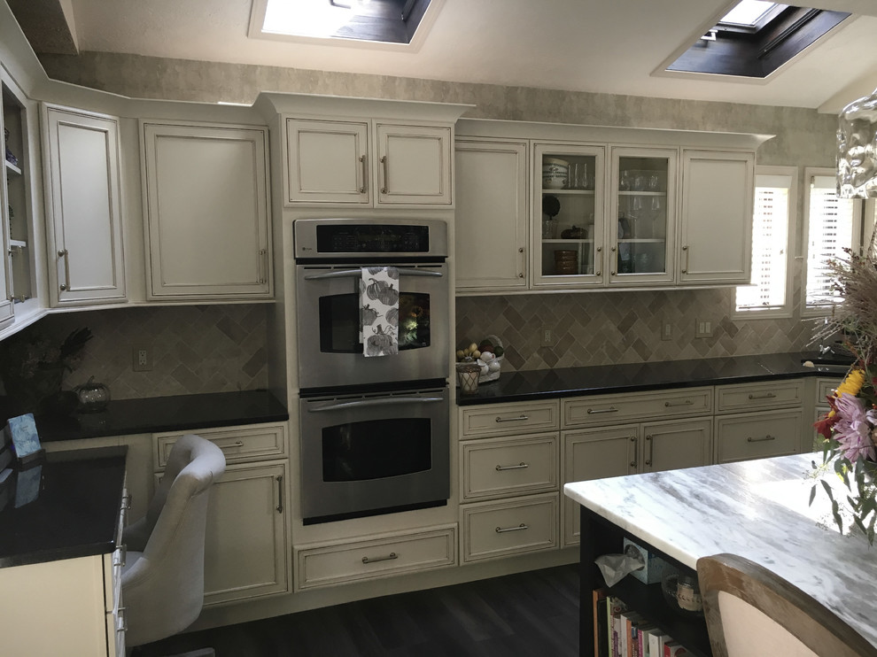 Example of a large transitional u-shaped laminate floor and gray floor eat-in kitchen design with an undermount sink, recessed-panel cabinets, white cabinets, granite countertops, white backsplash, ceramic backsplash, stainless steel appliances, an island and black countertops