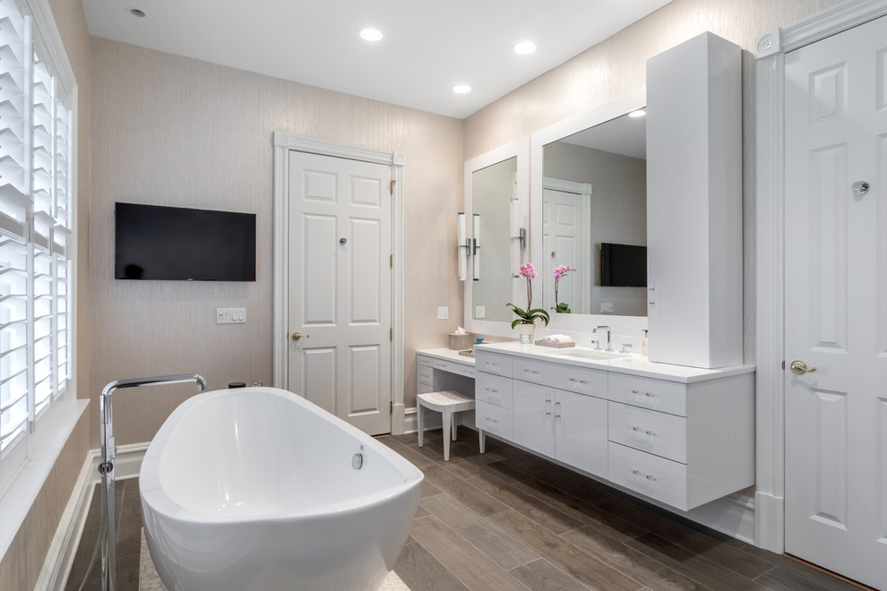 Inspiration for a mid-sized transitional 3/4 bathroom in New York with flat-panel cabinets, white cabinets, a freestanding tub, a one-piece toilet, beige walls, porcelain floors, an undermount sink and solid surface benchtops.