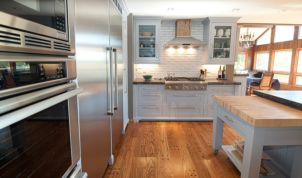 This is an example of a country eat-in kitchen in Other with grey cabinets, white splashback, stainless steel appliances, light hardwood floors and with island.