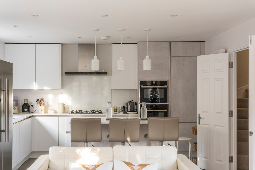 Inspiration for a mid-sized contemporary l-shaped open plan kitchen in London with flat-panel cabinets, grey cabinets, solid surface benchtops, grey splashback, glass sheet splashback, stainless steel appliances, medium hardwood floors, no island and brown floor.