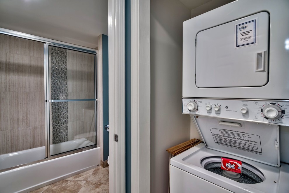 This is an example of a small transitional utility room in Miami with grey walls, ceramic floors, a stacked washer and dryer and brown floor.