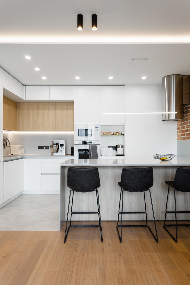 Photo of a mid-sized contemporary l-shaped open plan kitchen in Moscow with an undermount sink, flat-panel cabinets, white cabinets, solid surface benchtops, grey splashback, white appliances, porcelain floors, a peninsula, grey floor, grey benchtop and recessed.