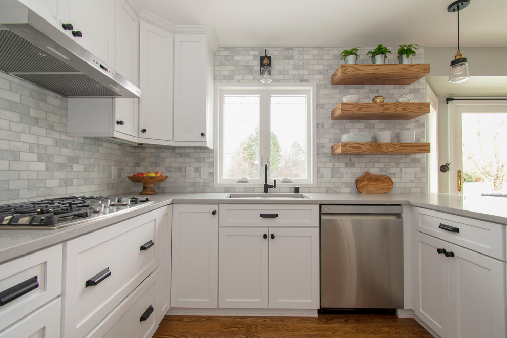This is an example of a mid-sized transitional u-shaped eat-in kitchen in Milwaukee with an undermount sink, shaker cabinets, white cabinets, quartz benchtops, grey splashback, marble splashback, stainless steel appliances, medium hardwood floors, a peninsula, brown floor and grey benchtop.