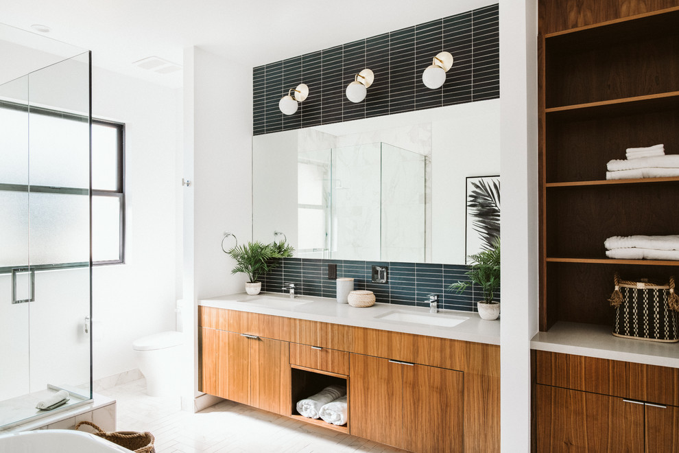 Beach style master bathroom in Los Angeles with flat-panel cabinets, medium wood cabinets, a corner shower, a one-piece toilet, ceramic tile, white walls, ceramic floors, an undermount sink, solid surface benchtops, white floor, a hinged shower door, beige benchtops and black tile.