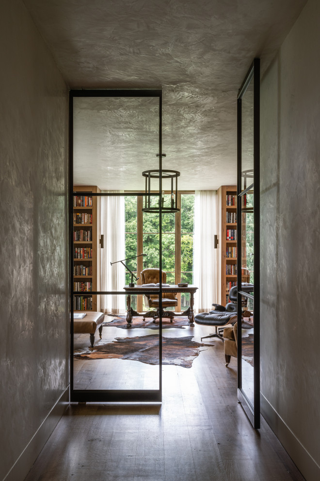 Пример оригинального дизайна: большой домашняя библиотека в стиле неоклассика (современная классика) с коричневыми стенами, паркетным полом среднего тона, отдельно стоящим рабочим столом, коричневым полом и деревянными стенами