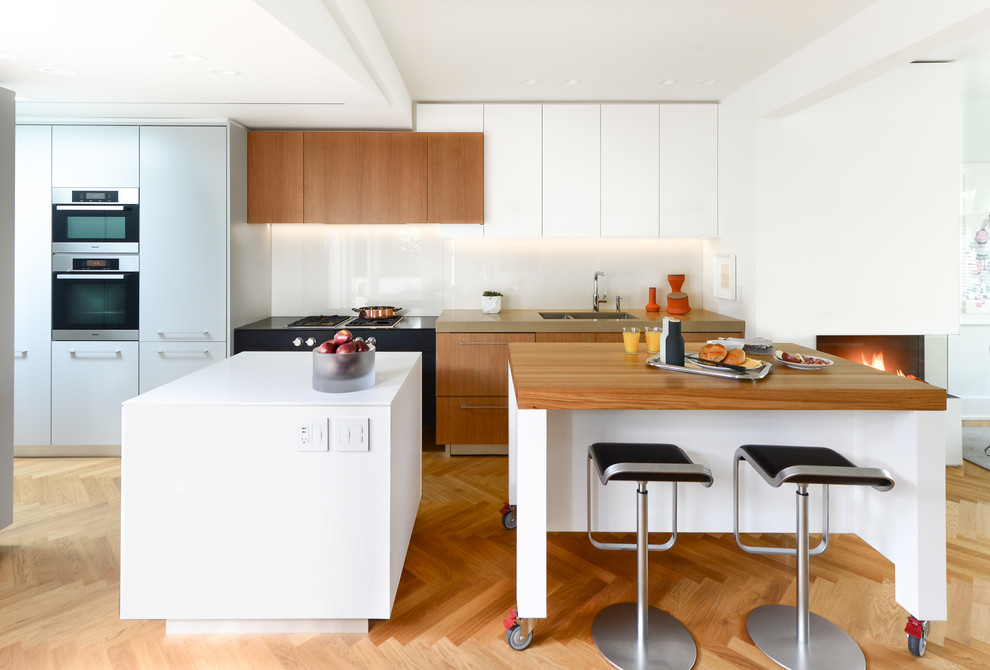 Inspiration for a mid-sized transitional single-wall open plan kitchen in Vancouver with a double-bowl sink, flat-panel cabinets, medium wood cabinets, quartz benchtops, white splashback, glass sheet splashback, stainless steel appliances, medium hardwood floors and multiple islands.